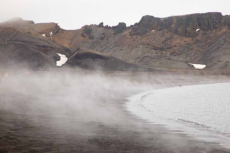 Hot water springs entering cold sea water over black sand beach in Antarctica.