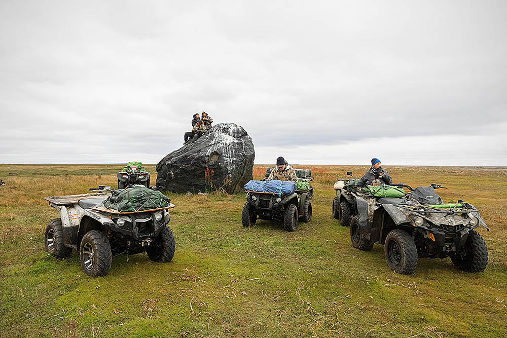 Quads or ATV's on the arctic tundra near large boulder, left by the last glacier, being used as a lookout point.