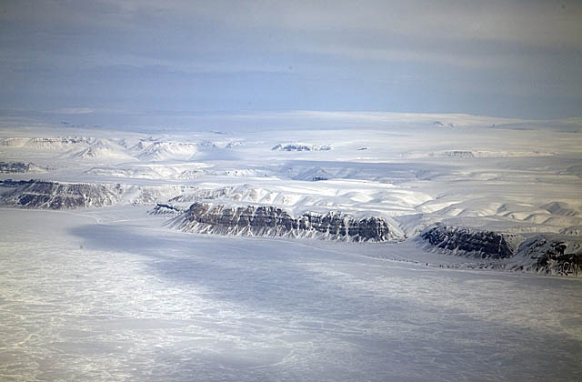 Aerial of snow covered seaside cliffs and sea ice.