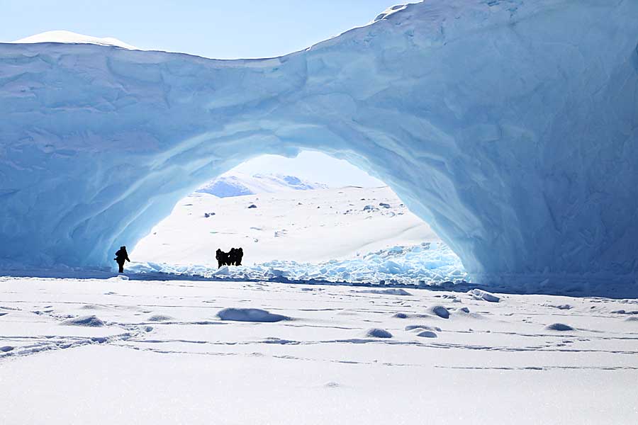 Ice formation with tourists standing under arch on sea ice near Baffin Island.