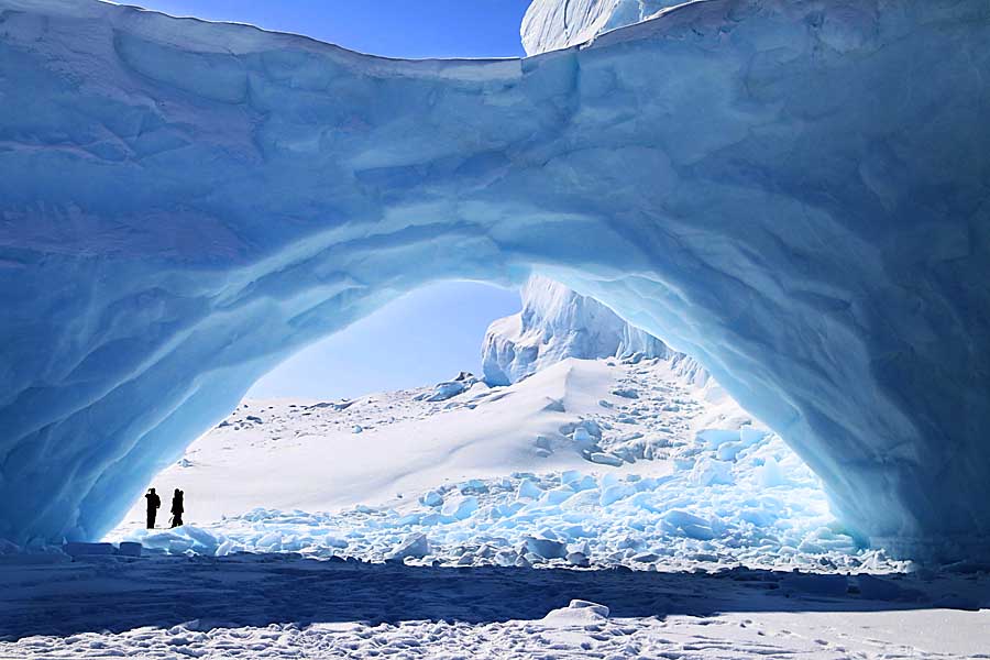 Ice formation with tourists standing under arch on sea ice near Baffin Island.