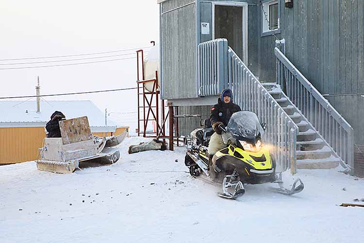 Inuit tour guide with snow mobile and tourist in sled.